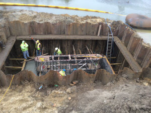 Crews stand inside a large hole beside the Middle River, which will serve as foundation for the bridge.